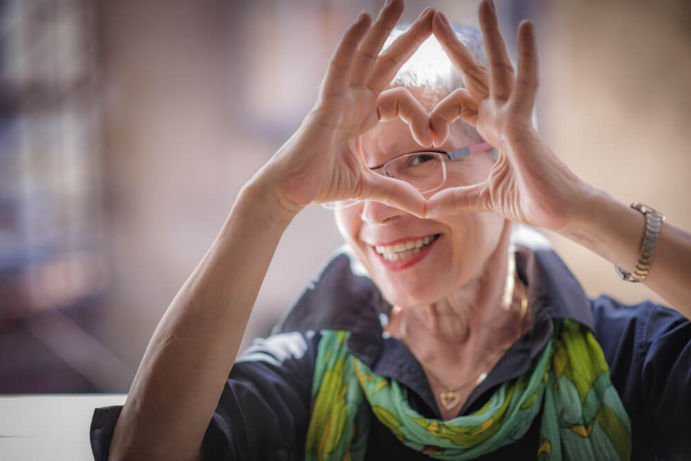 Happy older woman making a heart with her hands and looking through